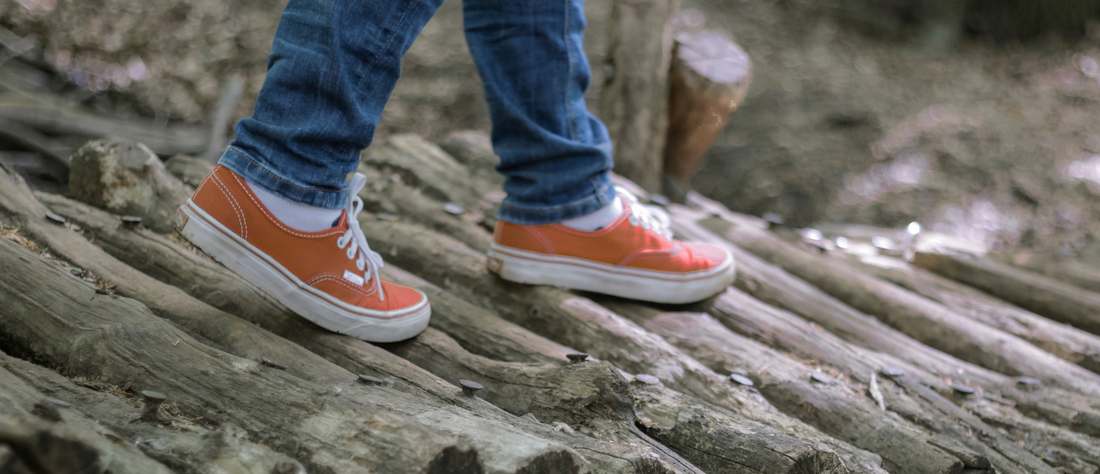 Les pieds d'un enfant en espadrilles corail, en équilibre sur un pont de rondins